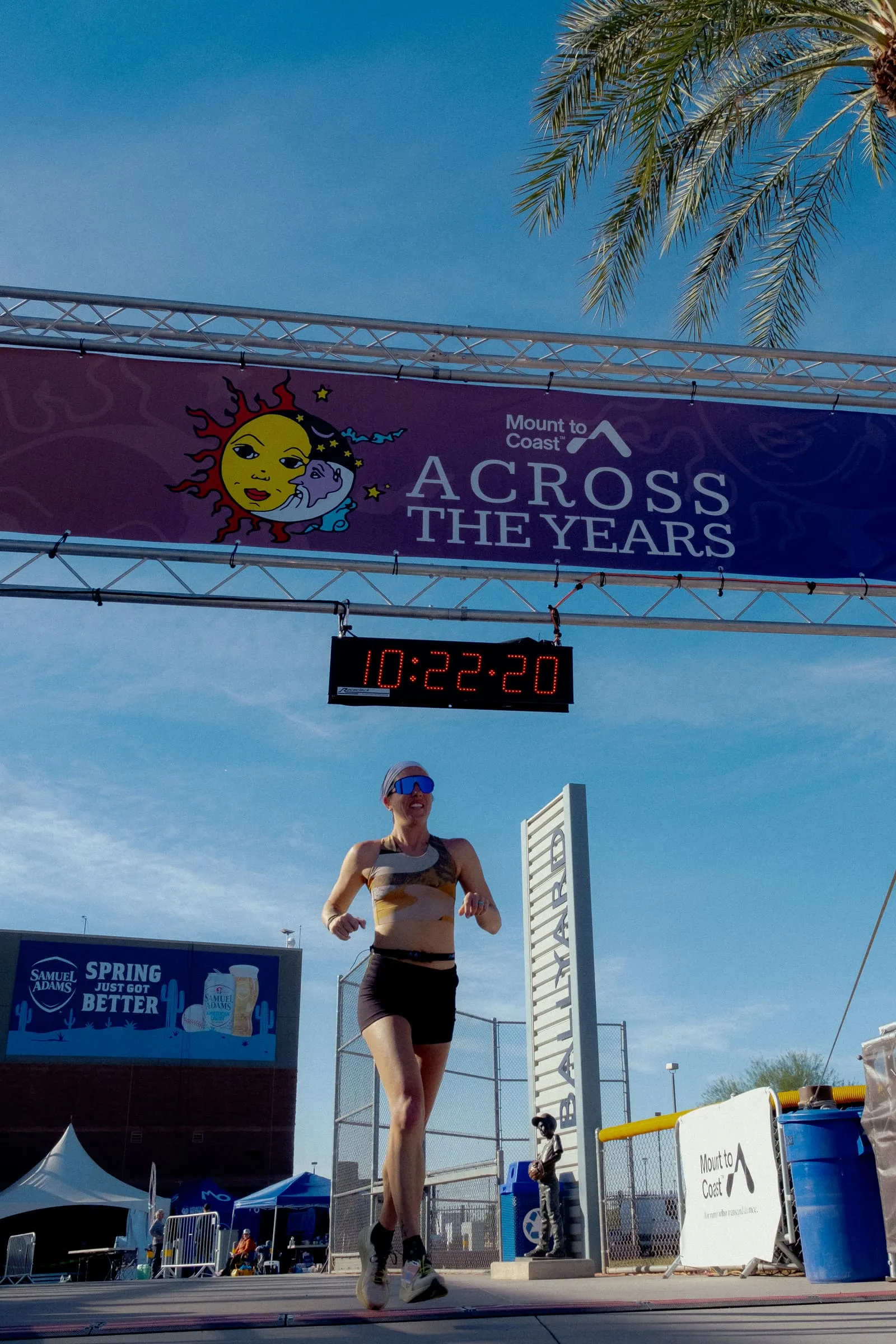 Megan Eckert running under the Mount to Coast Across the Years banner beneath a palm tree and blue sky