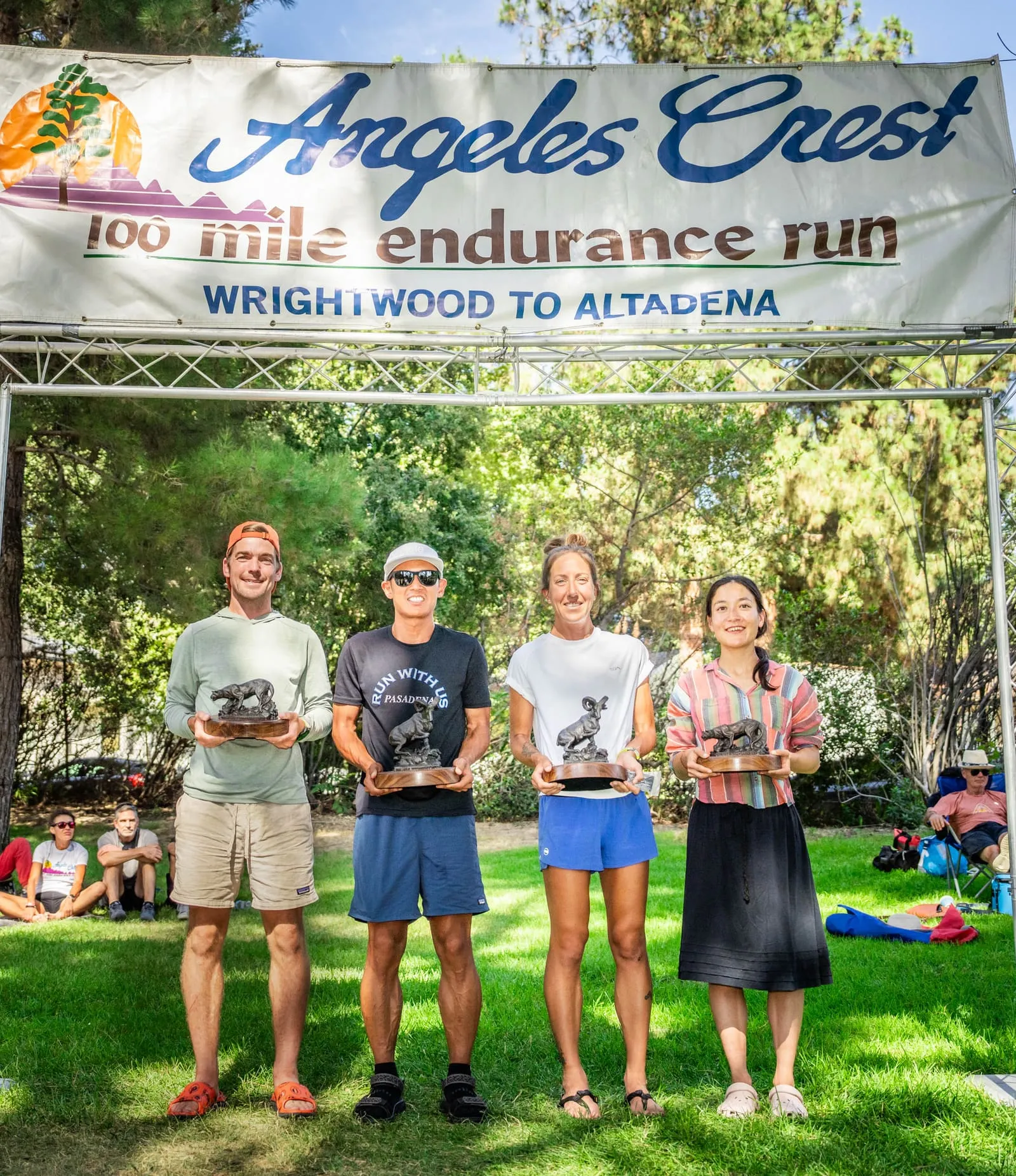 Megan Eckert holding a trophy with the other podium finishers under the Angeles Crest 100 finish banner