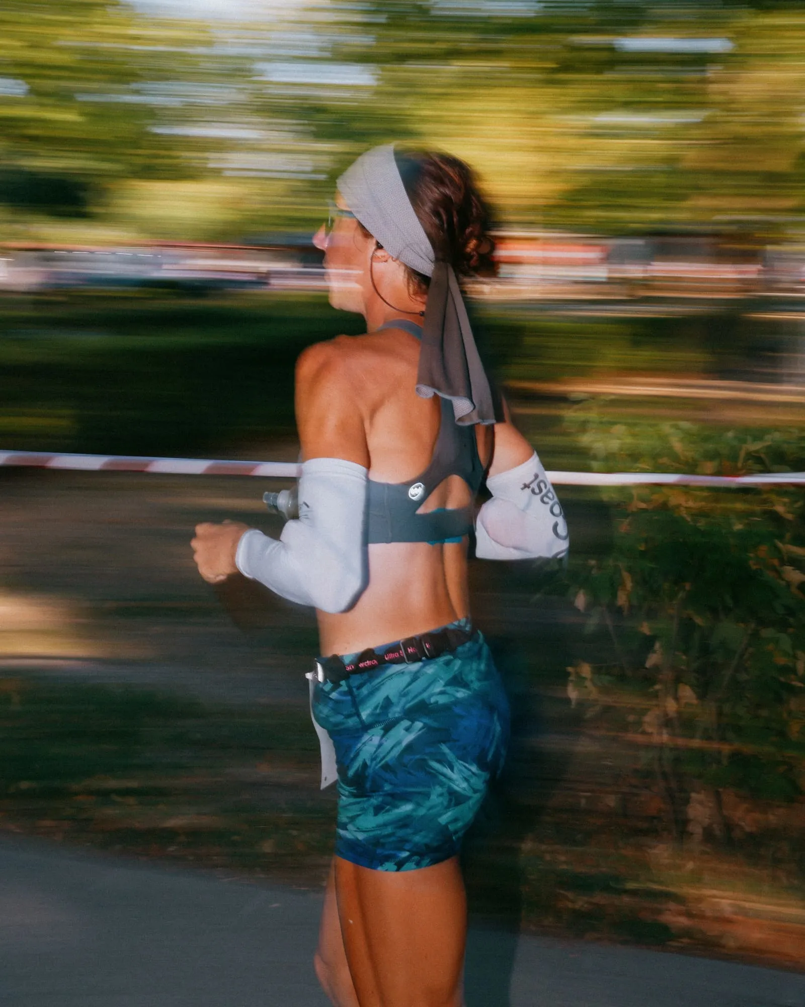 Motion-blurred photo of Megan Eckert running past the course tape in a headscarf and arm sleeves at the EMU 6-Day Race