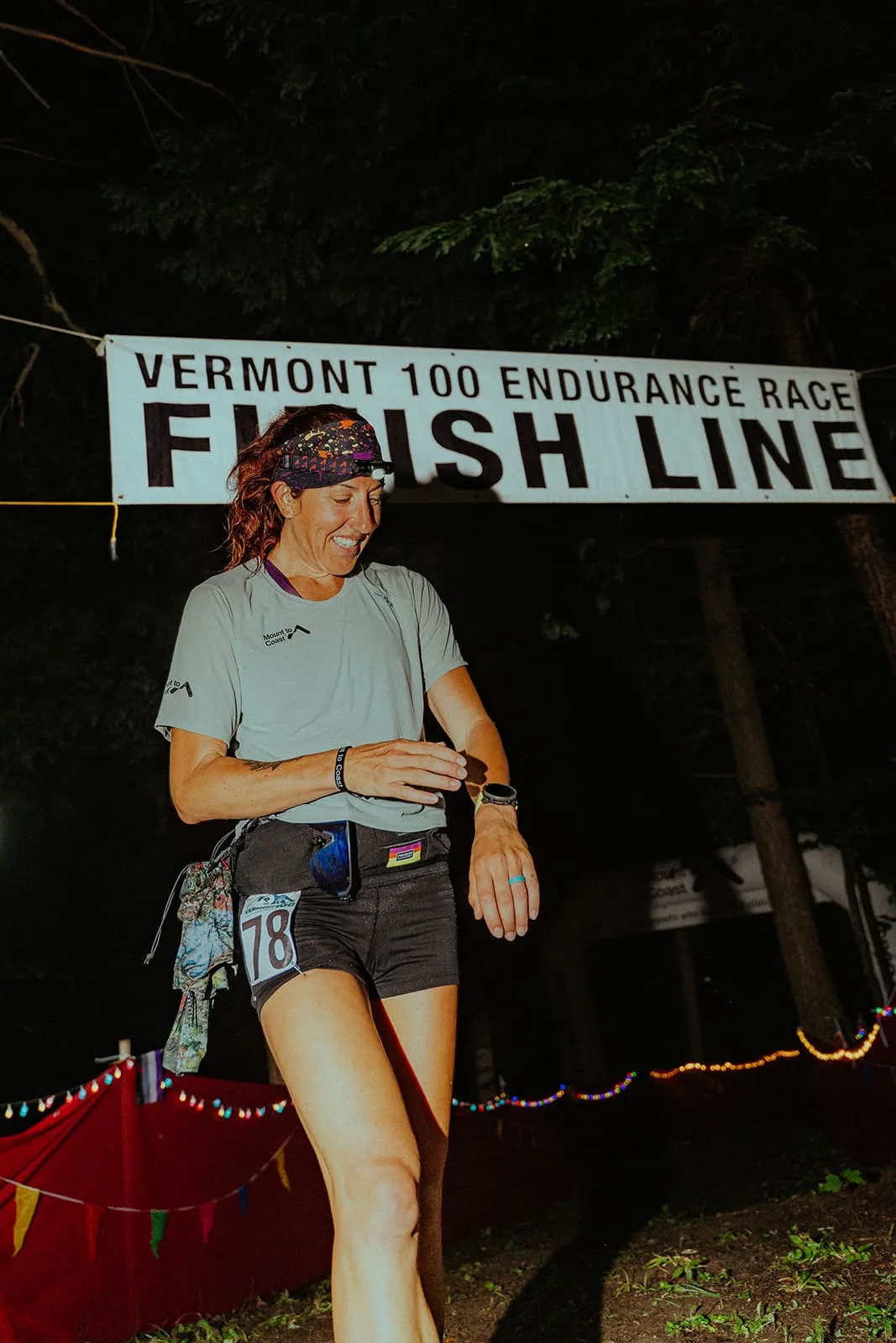 Megan Eckert smiling under the Vermont 100 Endurance Race finish line banner at night